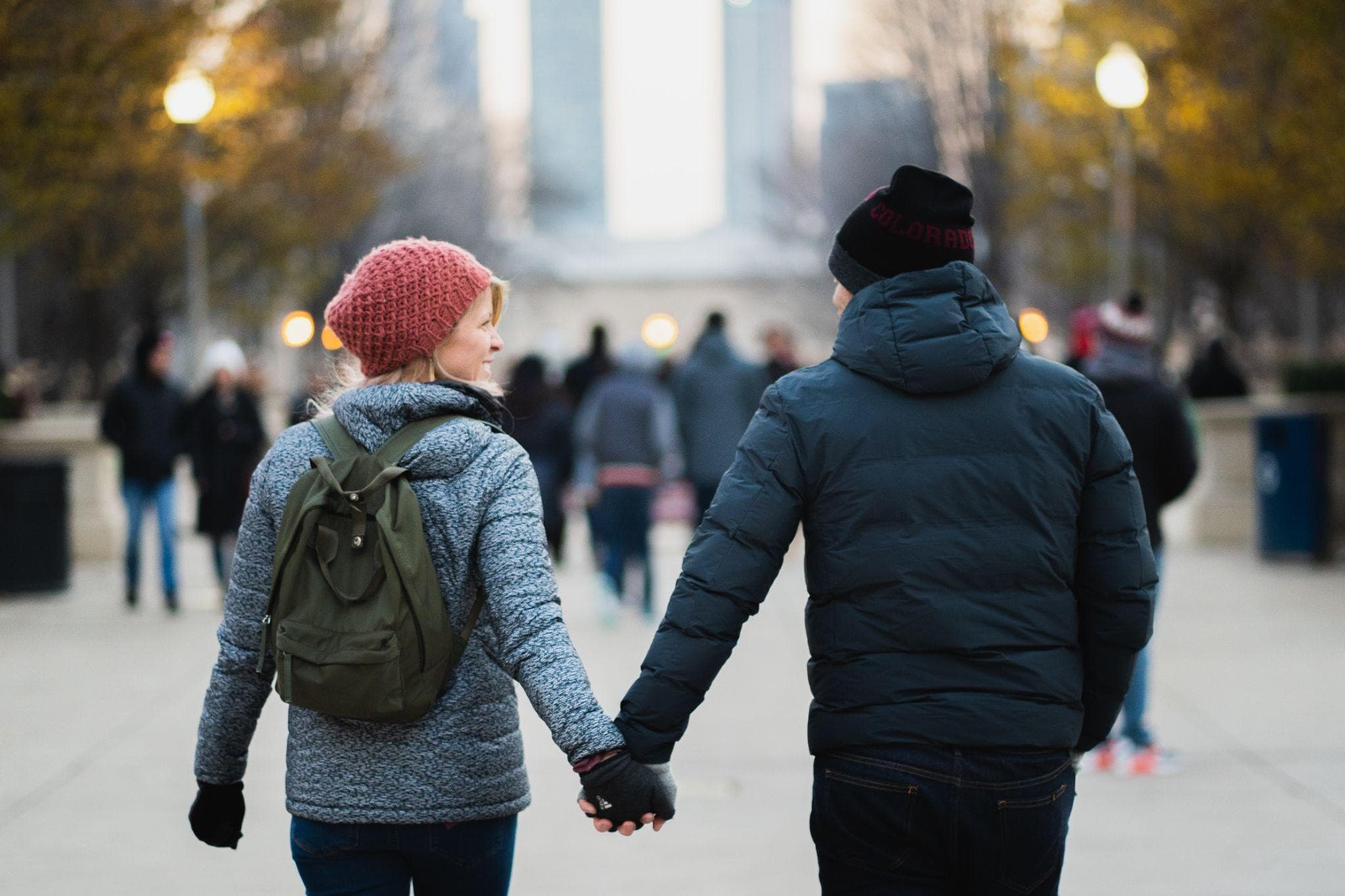 A man and woman holding hands, wearing winter clothing as they walk down a street